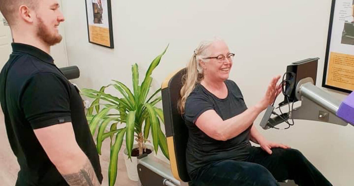 Äldre kvinna sitter på maskin hos OsteoStrong och ler