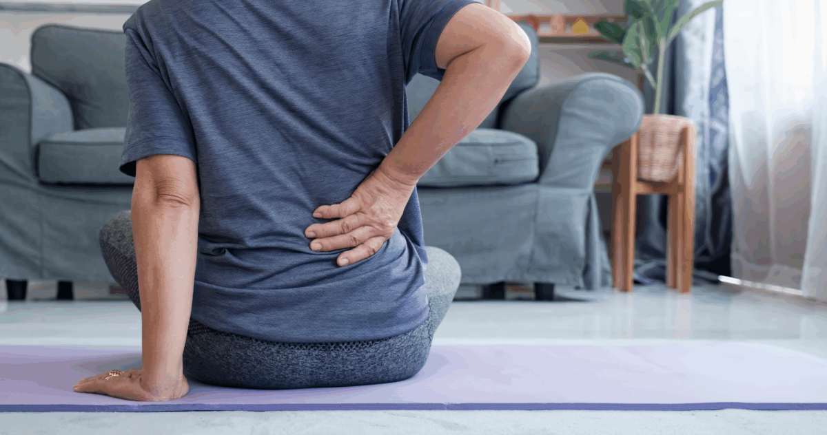 Äldre kvinna tar sig om höften sittandes på yogamatta