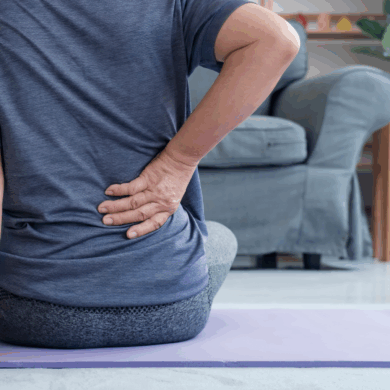 Äldre kvinna tar sig om höften sittandes på yogamatta